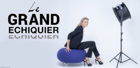 Anne-Sophie Lapix assise sur un pouf bleu sous un projecteur