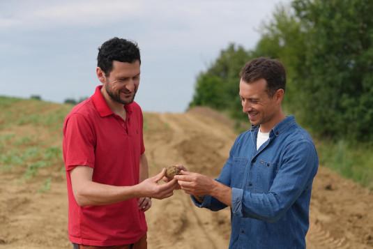 Jonathan Kirchner et Hugo Clément tenant un morceau de terre dans un champ