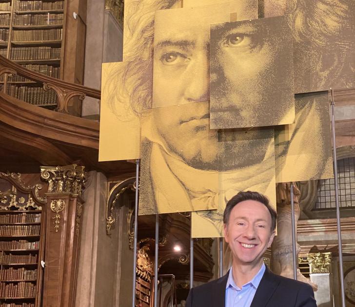 Stéphane Bern posant devant un portait de Ludwig van Beethoven