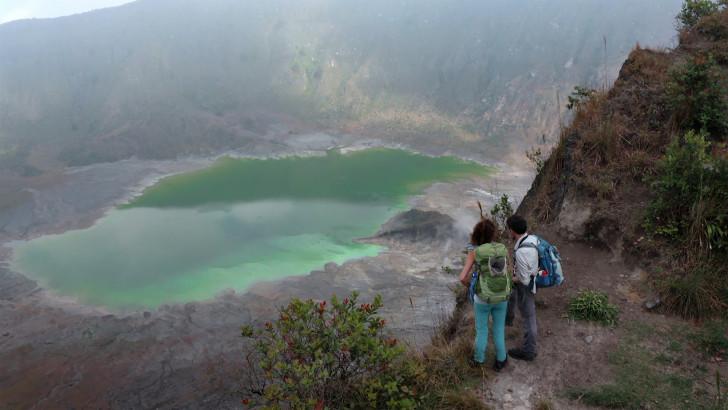 Deux randonneurs de tiennent face à un lac niché sur les pentes d'un volcan.